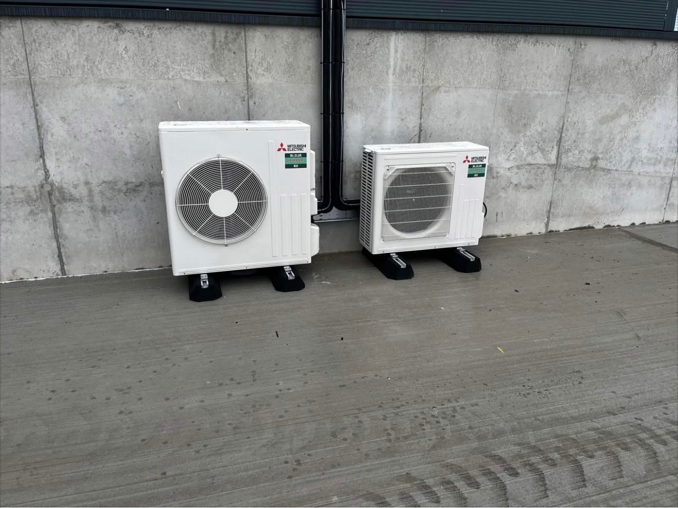 Two Mitsubishi Electric outdoor heat pump units installed on concrete plinths by Hall HVAC